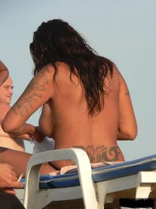 Topless tattooed lady on the beach with fake big tits