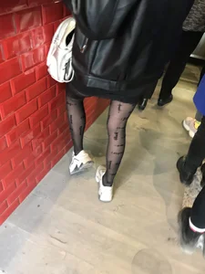 Sexy skinny legs in black pantyhose with dots and sneakers closeup creepshot in a cafe