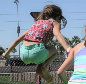 Brunette skinny teen in green shorts playing in a bounce house