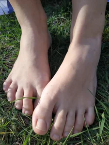 Candid girl with hot legs chilling on the grass in a park and showing off her feet