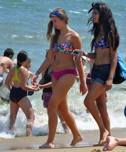 Hot beach brunette in shorts and bikini top with her friend in bikini