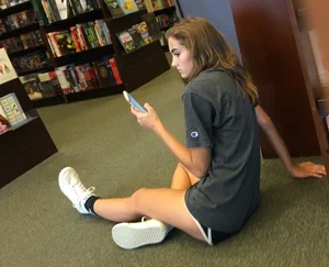 Cute skinny teen in shorts sitting on the floor at the book store