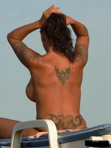 Topless tattooed lady on the beach with fake big tits