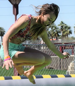 Brunette skinny teen in green shorts playing in a bounce house