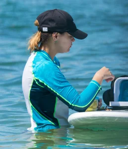 Girl in the water in a navy blue bikini bottom, shirt and hat with a nice ass