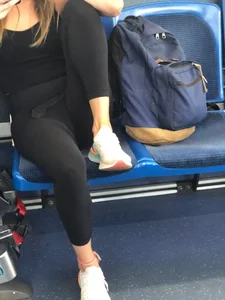 Young canid girl in leggings and sneakers sittin on a bus stop bending one leg street creepshot