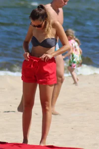 Hottie undressing from her red shorts to her bikini to layout on the beach