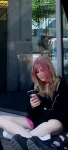 Awesome teen girl with pink dyed hair in hosrts sitting on the ground at the bus stop