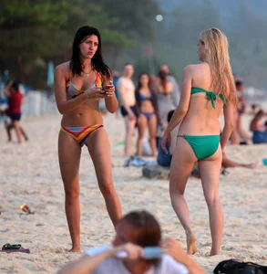 Sexy brunette in thong bikini and blonde friend in green bikini at the beach