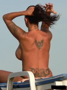 Topless tattooed lady on the beach with fake big tits