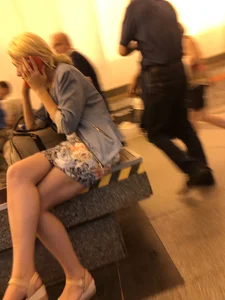 Candid girl in a skirt and sandals sitting with crossed legs at the subway station