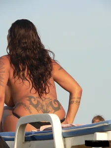 Topless tattooed lady on the beach with fake big tits