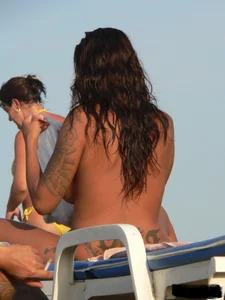 Topless tattooed lady on the beach with fake big tits