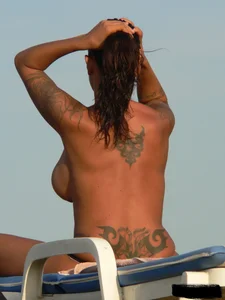 Topless tattooed lady on the beach with fake big tits