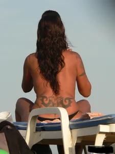 Topless tattooed lady on the beach with fake big tits