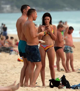 Sexy brunette in thong bikini and blonde friend in green bikini at the beach