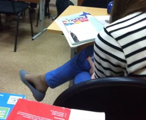 Young Candid Student Sitting With Crossed Legs, Flat Shoe Dangling on Her Foot in Pantyhose