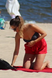 Hottie undressing from her red shorts to her bikini to layout on the beach