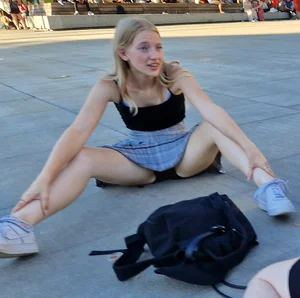 Young Skinny Girl in a Skirt Sitting With Legs Wide Apart on the Pavement, Flashing Her Panties