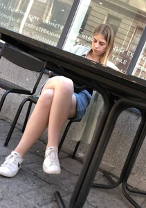 Cute candid girl sitting with crossed legs in a street cafe creepshot