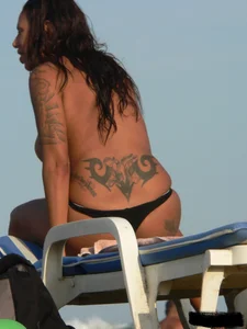 Topless tattooed lady on the beach with fake big tits