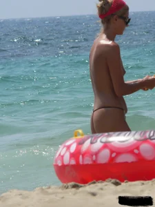 Topless skinny blonde lady in a g-string bikini at the beach