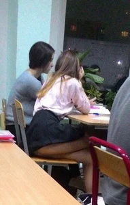 Hot College Teen in a Blouse and a Skirt Sitting at Her Desk With Crossed Legs Flashing Her Thigh
