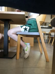 Legs of a skinny girl under a cafe table, wearing shorts, very pale skin