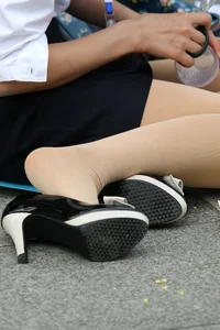 Candid girl sitting on asphalt wearing a skirt, pantyhose and shoes on high heels - with one shoe half taken off revealing her foot