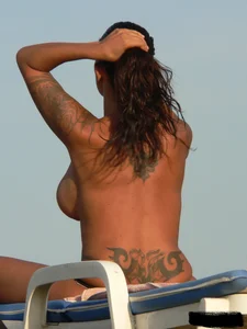 Topless tattooed lady on the beach with fake big tits