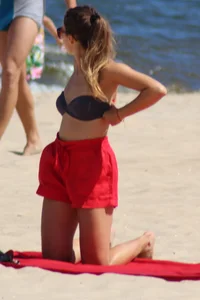 Hottie undressing from her red shorts to her bikini to layout on the beach