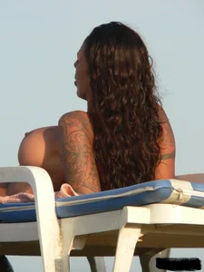 Topless tattooed lady on the beach with fake big tits