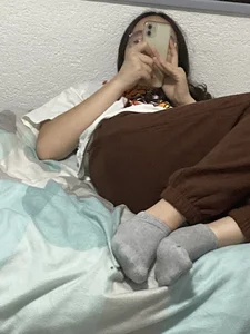 Cute Skinny Teen in Socks Lying in Bed With Her Smartphone