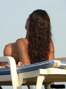 Topless tattooed lady on the beach with fake big tits