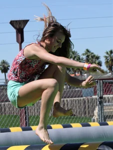 Brunette skinny teen in green shorts playing in a bounce house