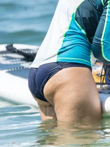 Girl in the water in a navy blue bikini bottom, shirt and hat with a nice ass