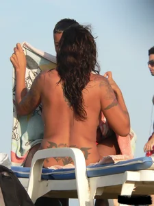Topless tattooed lady on the beach with fake big tits