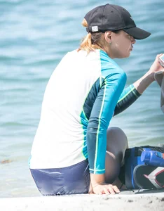 Girl in the water in a navy blue bikini bottom, shirt and hat with a nice ass