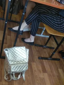 Crossed College Girl's Legs in Flats And Striped Pants Under a Desk in a Classroom