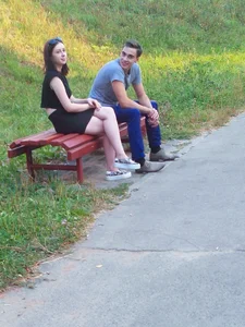 Cute young girl wearing a skirt sitting on the bench in the park with crossed legs