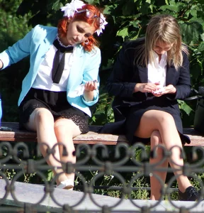 Girls in Skirts and Fishnet Stockings Sitting on the Bench in City Park