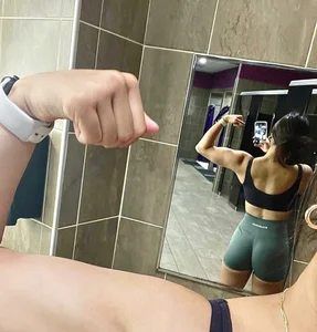 Sexy And Fit Girl in a Top And Spandex Shorts Showing Off Her Biceps in the Gym Locker Room Selfie