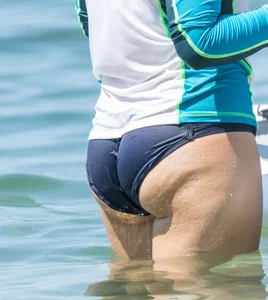 Girl in the water in a navy blue bikini bottom, shirt and hat with a nice ass