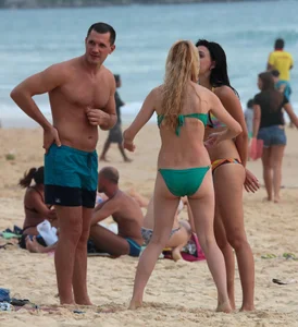 Sexy brunette in thong bikini and blonde friend in green bikini at the beach