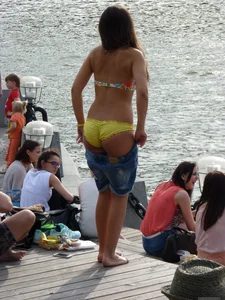 Cute Girl in Denim Shorts and Swimsuit Undressing on the Riverbank Candid Photo