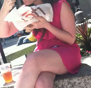Girl in a short dress eating fast food on the street, crossed chunky legs