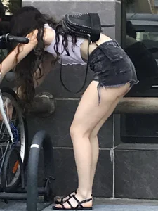 Pale girl in a top and denim mini shorts with awesome long legs in sandals bending over on the street