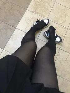 College teen girl's skinny legs in black pantyhose closeup with her sneakers taken off, nice feet