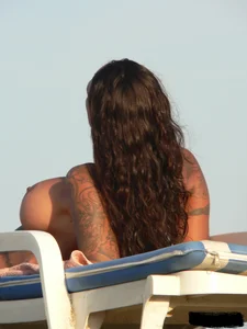 Topless tattooed lady on the beach with fake big tits