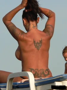 Topless tattooed lady on the beach with fake big tits